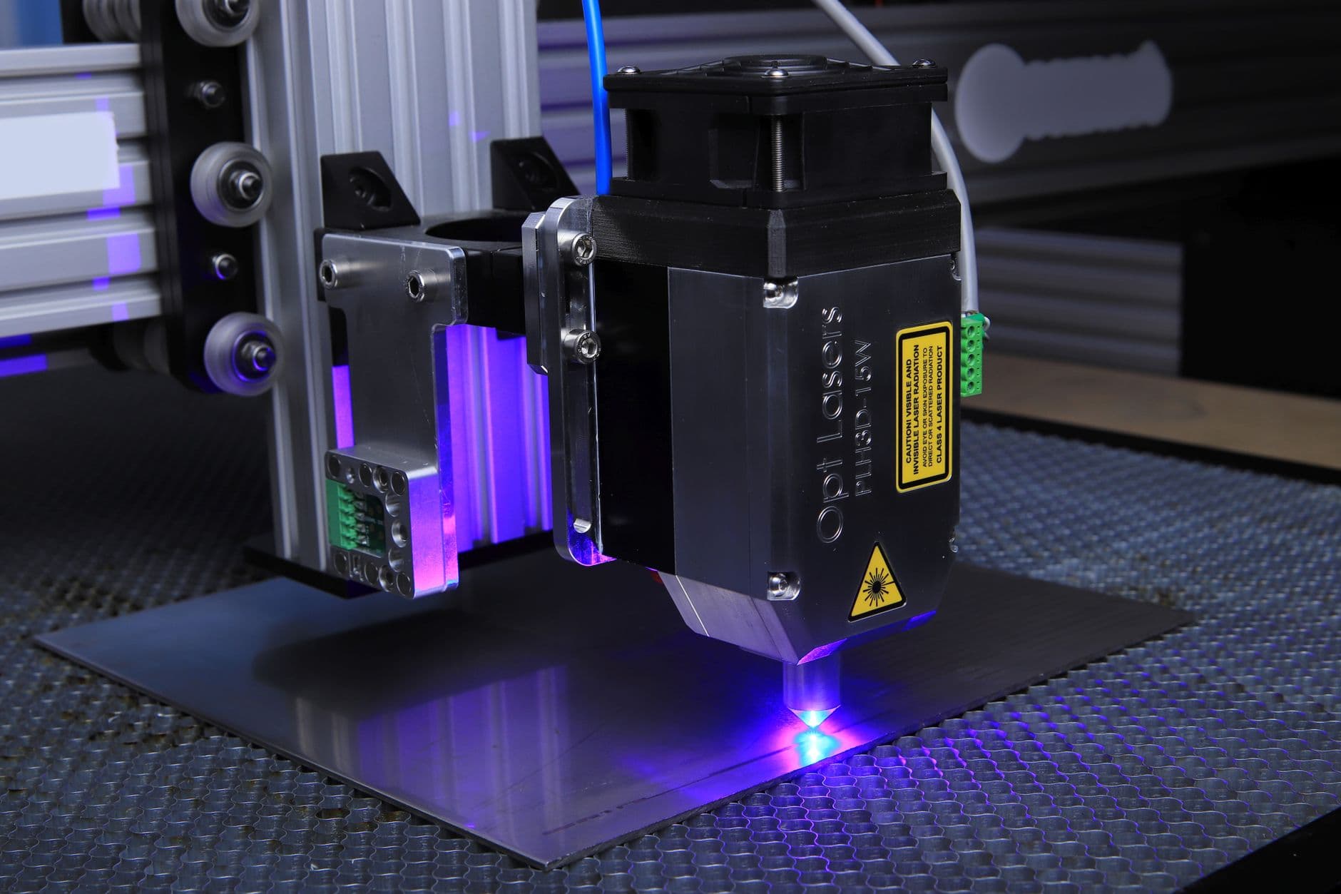 A blue diode laser head cutting a metal sheet on a honeycomb bed